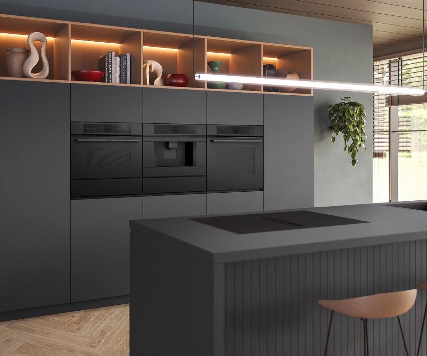 Moderne Küche mit mattgrauen Schränken, Einbaugeräten, offenen Regalen mit Dekoartikeln, einer großen Kücheninsel mit Spüle, einem Induktionskochfeld, zwei Barhockern aus Holz, einer Pendelleuchte und einem Fenster mit Blick auf einen begrünten Hinterhof.